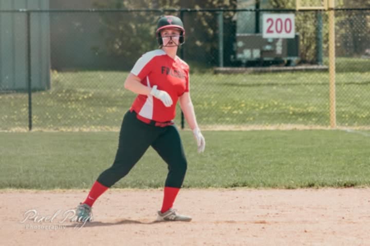 Emily in red and black softball uniform running on a dirt field with a chain-link fence and "200" sign in the background.