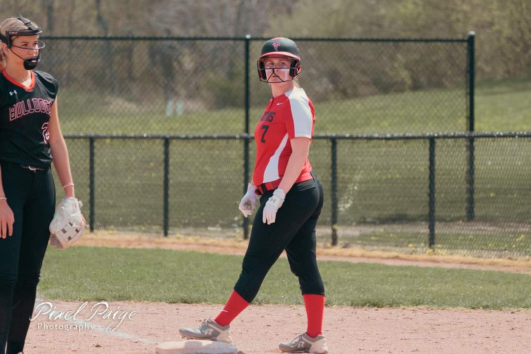 Emily in red and black uniform stands on base, another player in black uniform nearby on the field.