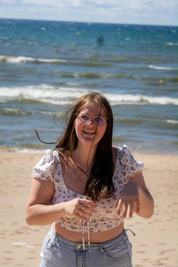 Emily smiling on a sunny beach with waves in the background.