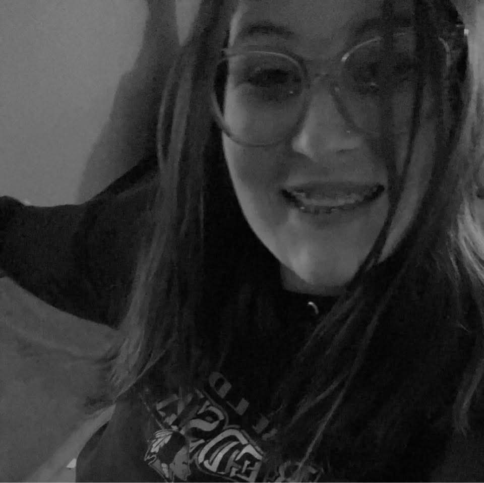 Black-and-white close-up of Emily with glasses and braces, wearing a hoodie with text.